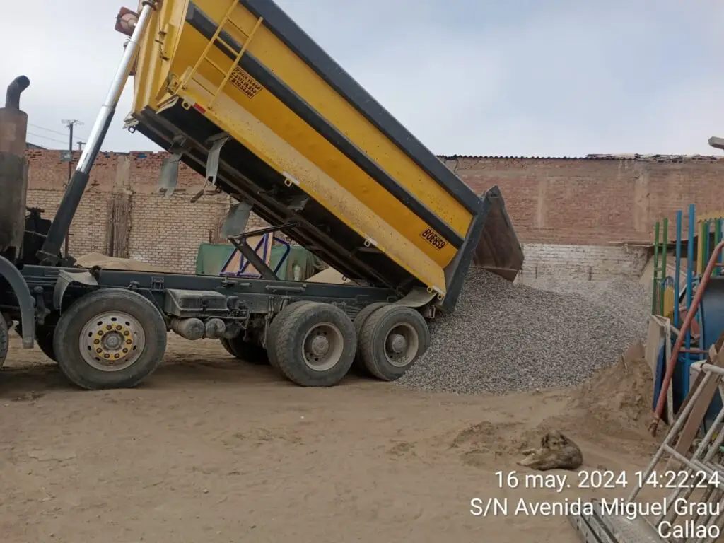 Volquete cien pies de color amarillo descargando piedra chancada de media pulgada en almacén ubicado en el Callao, Perú.