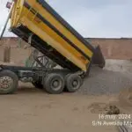 Volquete cien pies de color amarillo descargando piedra chancada de media pulgada en almacén ubicado en el Callao, Perú.