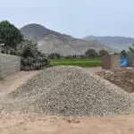 Montículo de piedra chancada en un terreno abierto con montañas y áreas verdes al fondo. Material de construcción utilizado en obras civiles y pavimentación.