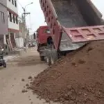 Volquete doble eje rojo haciendo descarga de tierra de chacra en calle de Lima, Perú