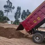 Volquete doble eje rojo descargando tierra de chacra en área campestre de Lima, Perú