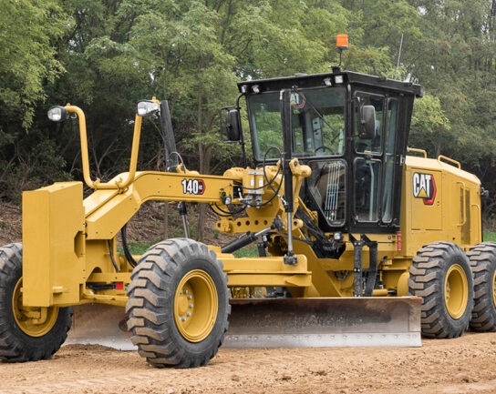 Motoniveladora amarilla Caterpillar 140 operando en un terreno de tierra, rodeada de árboles. Máquina pesada utilizada para nivelar y perfilar superficies en construcción.